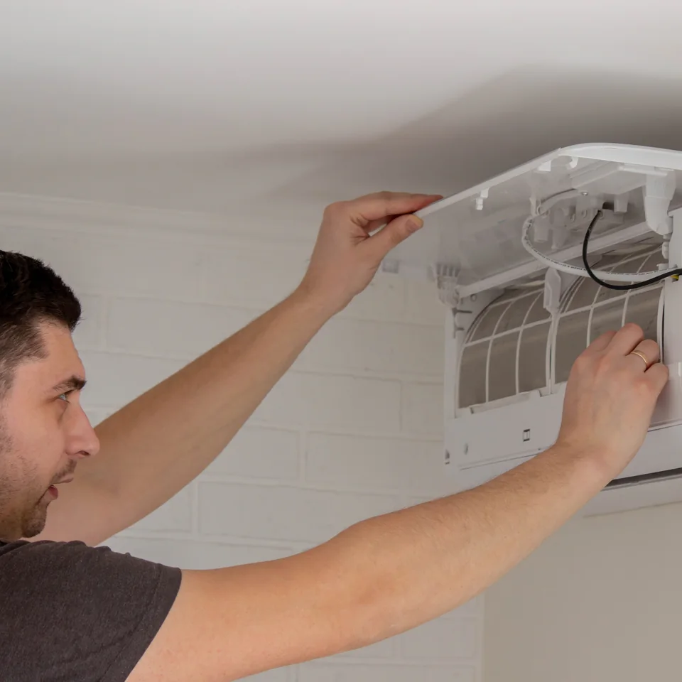 Technicien contrôlant les filtres d’un climatiseur mural dans un logement