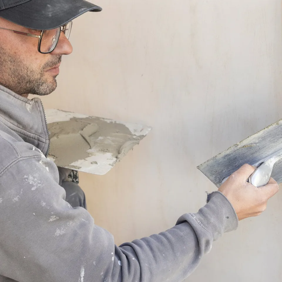 Artisan en veste grise appliquant de l’enduit sur un angle de mur