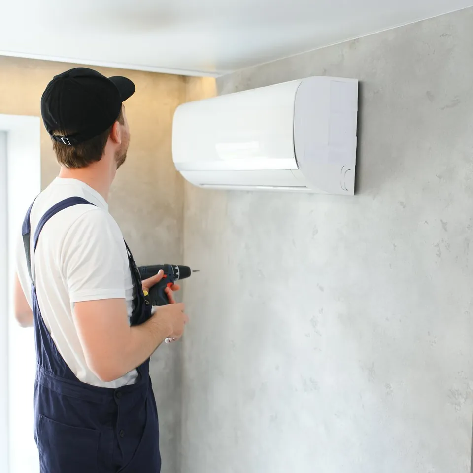 Artisan intervenant sur un climatiseur mural dans une pièce en cours de rénovation